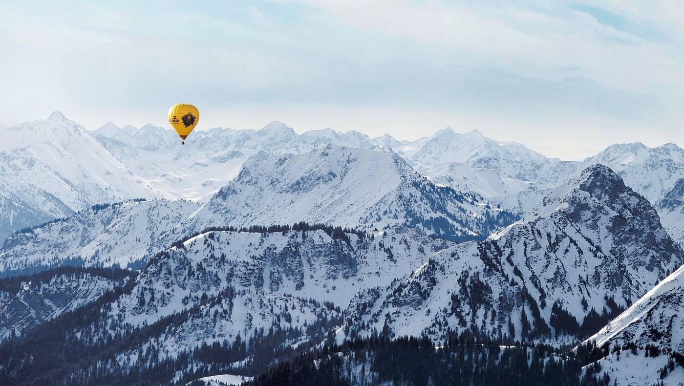 Ein gelber Heißluftballon, dahinter die schneebedeckten Alpen