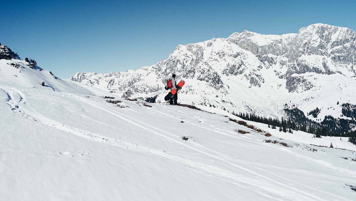 Ein Snowboarder steht in der Winterlandschaft mit Blick auf den Hochkönig.
