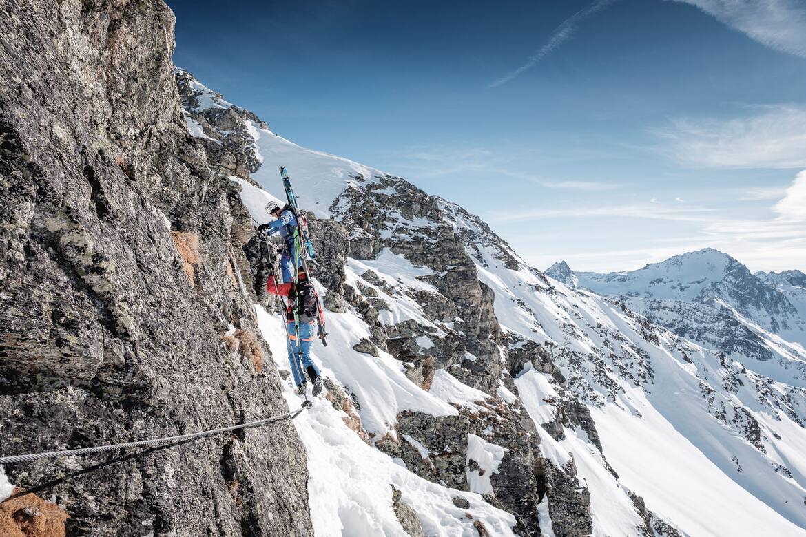 Ein Stahlseil in Fels und Schnee: Mit Skiern am Rücken und Skischuhen an den Füßen geht es am Arlberger Winterklettersteig am Rendl in Richtung Rossfallscharte.
