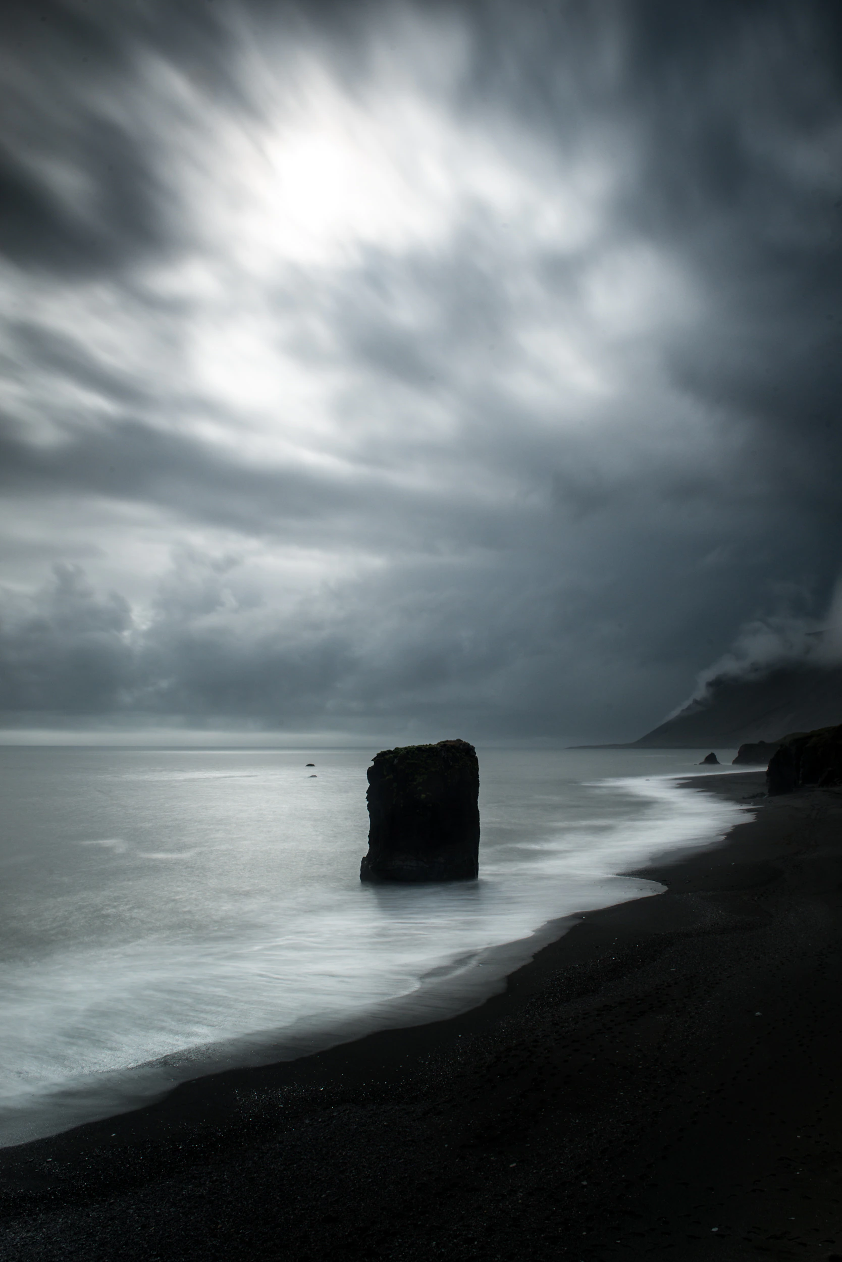 Ein einsamer Felsturm im Meer am schwarzen Strand  