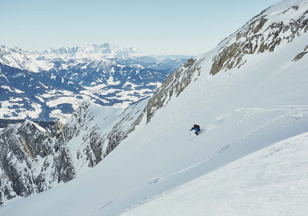 Ein Skifahrer bei der Abfahrt in einer Rinne, dahinter der Alpenhauptkamm.