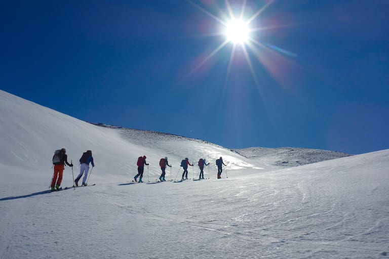 Ein Gruppe von Skitourengehern auf einem Firnspiegel: Die glänzende Spiegelfläche reflektiert das Sonnenlicht