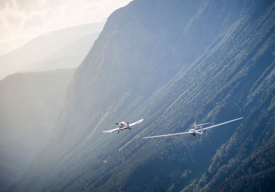 Zwei Flugzeuge vor nebelverschleierten Bergen.