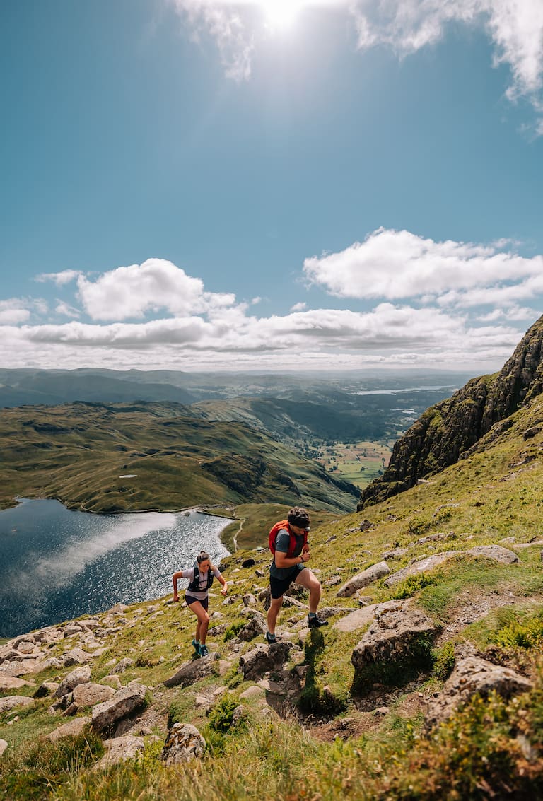 Trailrunner rennen auf einem Berg, im Hintergrund ist ein See zu sehen