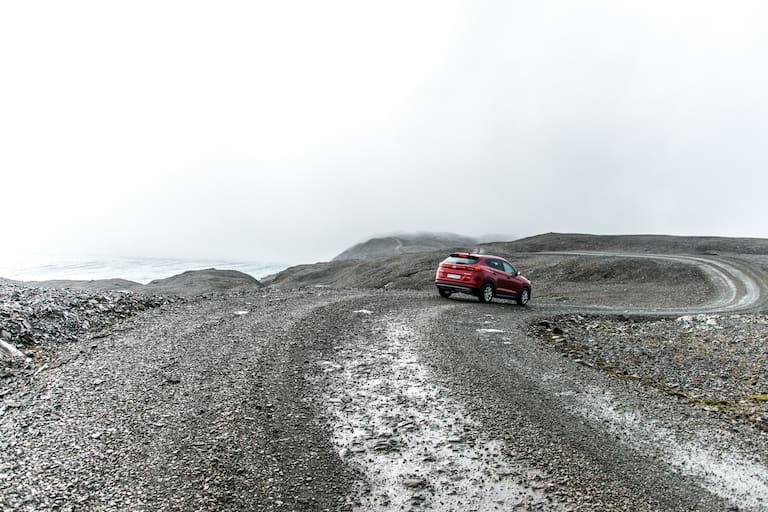 Rotes Auto auf isländischer Bergstraße bei nebligem Wetter 
